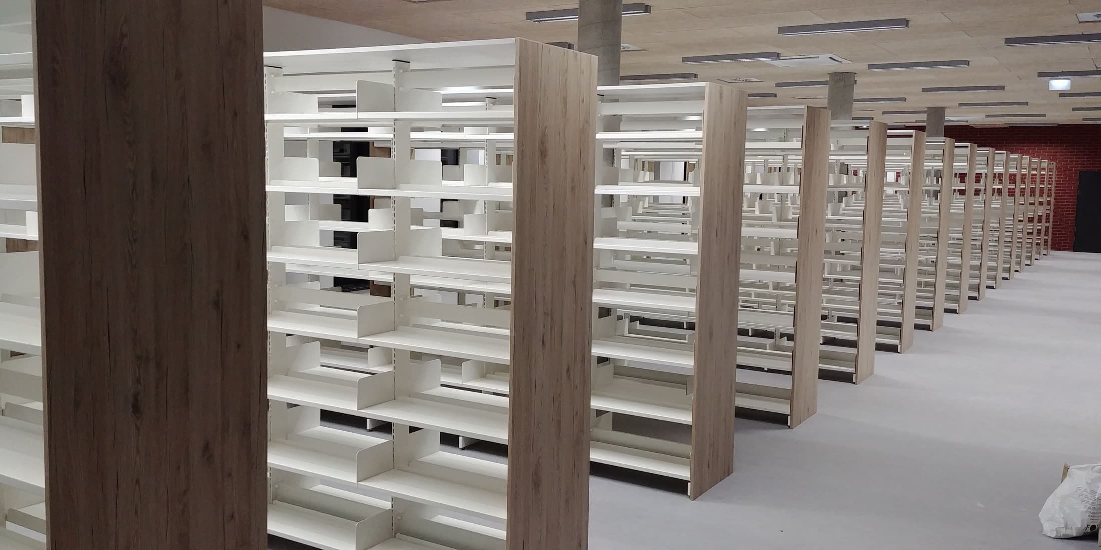 Długie ciągi regałów bibliotecznych z białymi półkami i drewnianymi panelami bocznymi